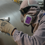 Operario realiza soldadura láser sobre tanque de acero inoxidable, usando equipo de protección personal completo, en planta industrial de Grupo Lassen